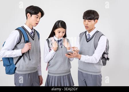 A group of high school students in uniform are looking at a mobile phone together. Stock Photo