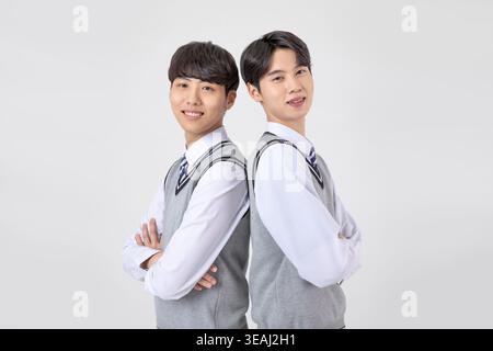 Two young Asian men in school uniforms stand back-to-back, smiling and looking at the camera. Stock Photo