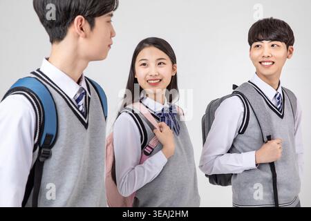 Three high school students in uniforms, smiling and chatting together. Stock Photo