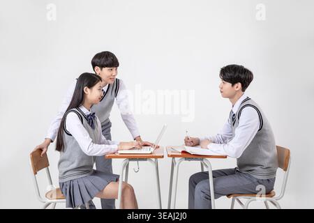 A group of high school students in school uniforms work together on a project using a laptop in a classroom. Stock Photo