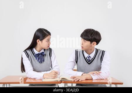 Two students in school uniforms sitting at a desk, studying together and looking at each other. Stock Photo