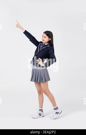 A young schoolgirl stands in a dynamic pose, pointing her finger in the air. Stock Photo