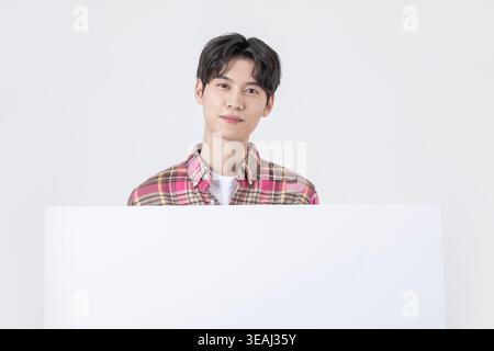 A young Asian man looks directly at the camera with a neutral expression in a blank white background. Stock Photo