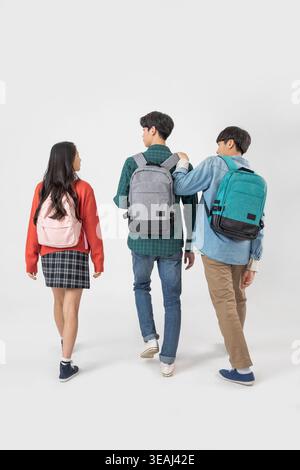 A group of young students, all wearing backpacks, walk together in a casual, relaxed manner. Stock Photo