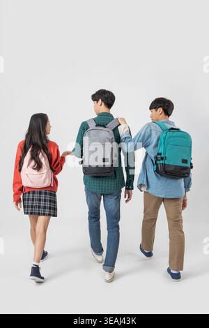 Three students, one male and two female, walking together, carrying backpacks and wearing casual school attire. Stock Photo