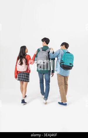 Three students walking together, wearing backpacks, against a white background. Stock Photo