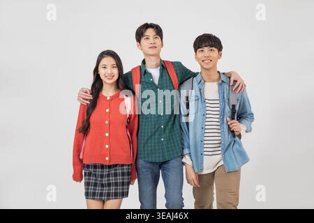 Three smiling high school students from different ethnicities walk together, arms around each other, on a sunny campus. Stock Photo