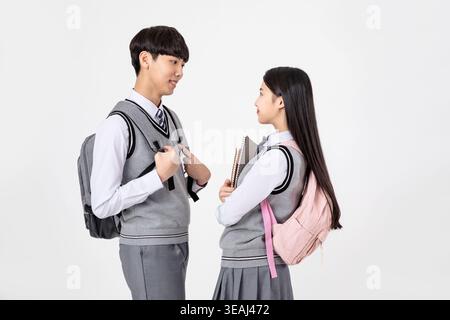 Two high school students in uniform are standing and talking to each other in a school hallway. Stock Photo
