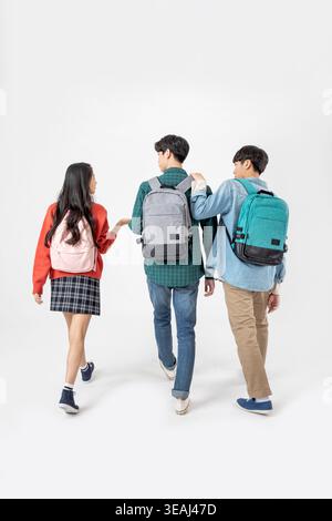 Three students walk together, wearing backpacks, in a neutral setting. Stock Photo