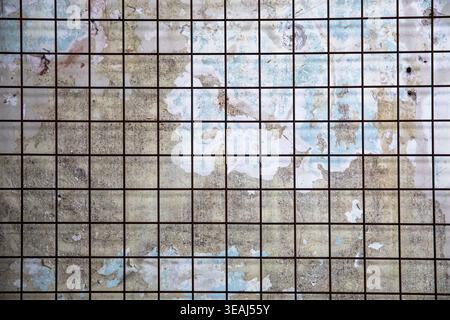 A weathered, rusty metal grid is exposed on a crumbling, ancient, stone wall. Stock Photo
