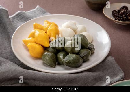 A plate of songpyeon tteok (Korean rice cakes) in various colors, including yellow, green, and white, sits on a tablecloth. Stock Photo