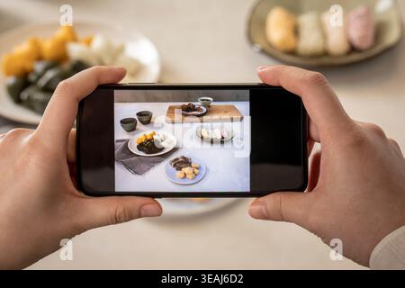 A person's hands hold a smartphone, displaying a food image on the screen. Stock Photo