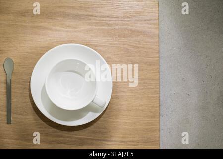 A white cup sits on a wooden table next to a spoon. Stock Photo
