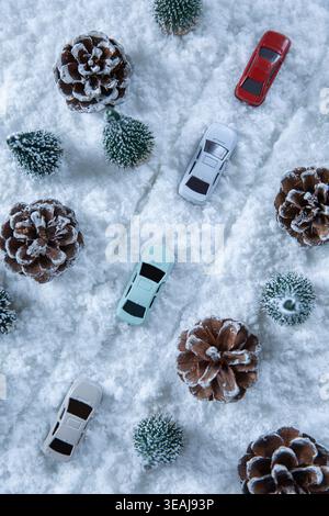 Small toy cars are scattered among snow-covered pinecones and evergreen trees in a winter wonderland setting. Stock Photo