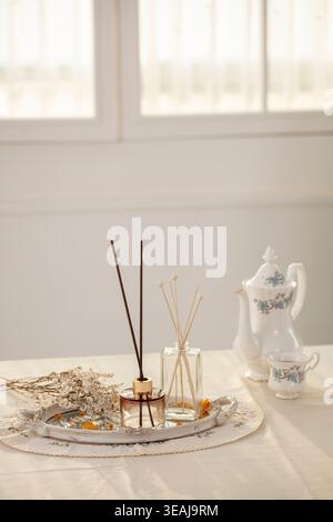 A delicate glass tray on a table in a white room, holding various scented reed diffusers and a few dried flowers. Stock Photo