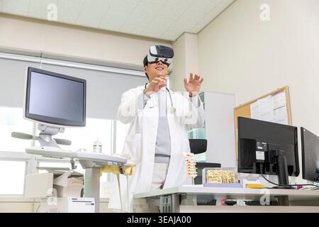 A doctor wearing a virtual reality headset in a medical office, exploring medical imagery. Stock Photo