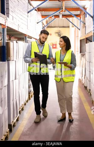 Warehouse workers talking, walking through stockroom aisle Stock Photo