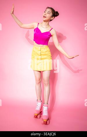 A young woman in a pink top and yellow skirt is standing on roller skates, holding her arms out to the side. Stock Photo