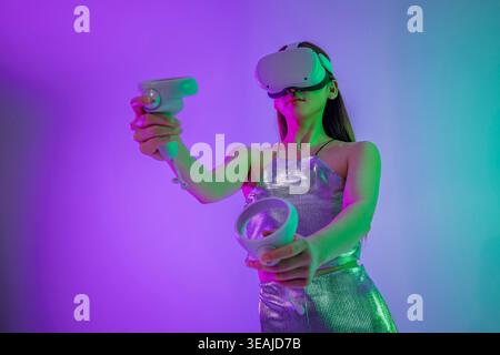 A woman in a futuristic outfit plays a VR game, immersed in a virtual world. Stock Photo
