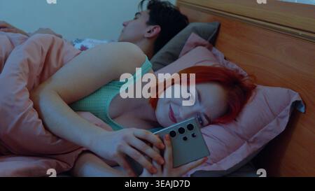 Young couple using smartphones while lying in bed at night Stock Photo