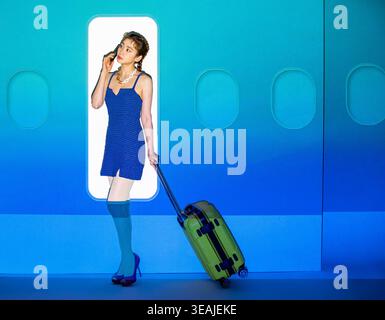 A young woman stands in front of a plane door, holding a suitcase and speaking on her phone. Stock Photo