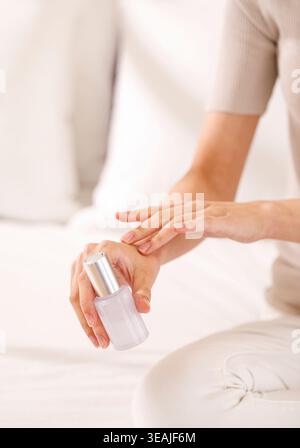 A woman is gently applying nail polish to her hands on a white couch. Stock Photo