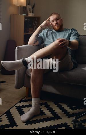 Portrait of Adult Man Sitting with Ankle Monitor in Home Confinement Stock Photo
