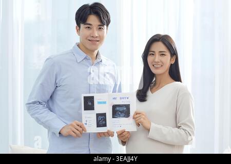 A young couple is holding an ultrasound photo album, smiling and looking happy. Stock Photo