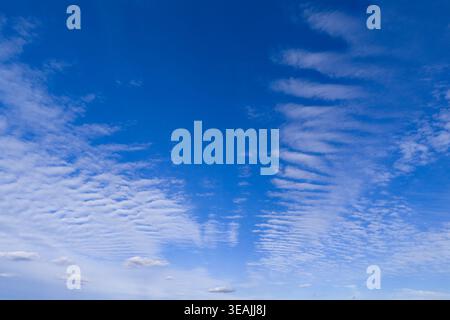 Blue sky with fluffy clouds wallpaper. Scattered white clouds in a clear blue sky. Cloud texture and light gradients. Sun shining through puffy clouds Stock Photo