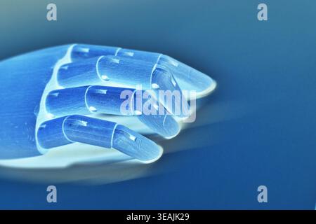 Close-up side view of a neon blue robotic hand isolated against a blue background in a monochromatic futuristic style. The image emphasizes artificial Stock Photo
