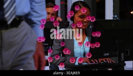 Smiling woman, gray blazer blouse, typing in call center night, with headsets monitors pink overlay Stock Photo