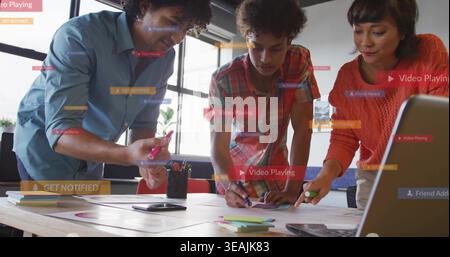 Leaning colleagues in blue shirt, plaid and orange sweater reviewing mockups at office, UI labels Stock Photo