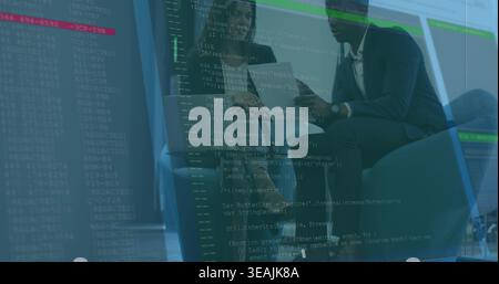 Reviewing two colleagues pointing at laptop and tablet in office lounge with code overlay, in suits Stock Photo