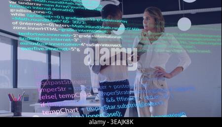 Discussing two women in biz-casual clothes viewing smartphone and laptop in office, code overlay Stock Photo