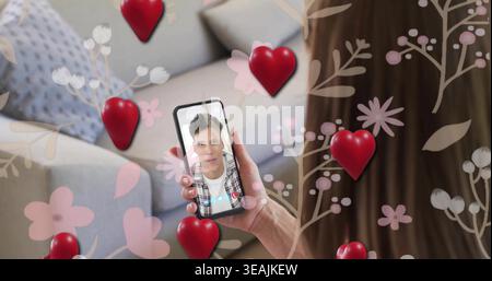 Holding smartphone, woman watching man speaking on call in living room, with red hearts Stock Photo