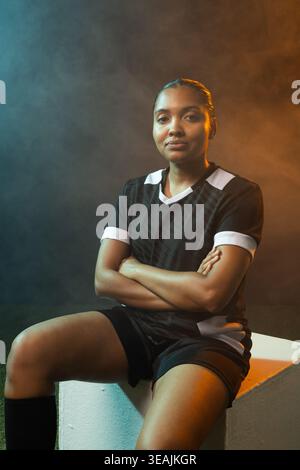 Woman sitting on white cube in studio wearing black jersey, knee-high socks, haze creating gradient Stock Photo