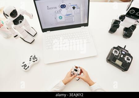 A person sits at a desk surrounded by various robot toys and a laptop screen displaying an AI education website. Stock Photo