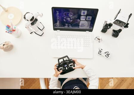 A person is sitting at a desk, surrounded by various robotic toys and devices, working on a laptop with a screen displaying a character characterizing app. Stock Photo