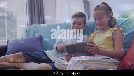 Holding tablet girl in yellow ruffled top and striped pants, boy leaning on teal sofa, overlays Stock Photo