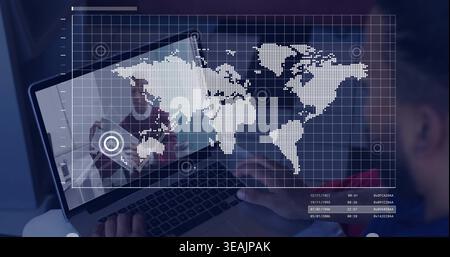 Displaying laptop with world map overlay, grid and markers at desk, colleague in red top typing Stock Photo