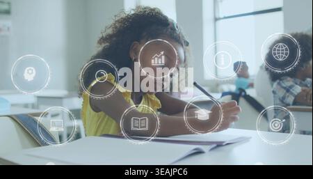 Writing child wearing sleeveless yellow top using pencil on open notebook at classroom desk, icons Stock Photo