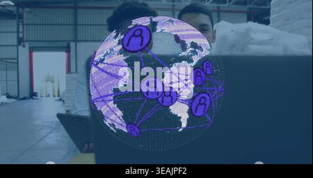 Analyzing colleagues wearing casual work shirts studying holographic globe on laptop in warehouse Stock Photo