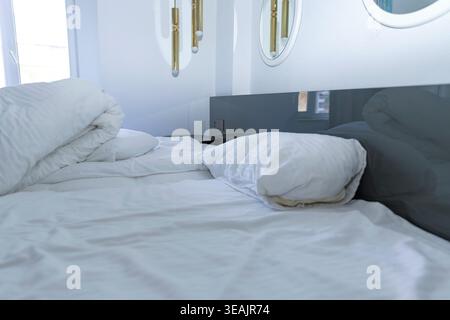 Unmade bed with white bedding and pillows in modern bedroom interior close view Stock Photo