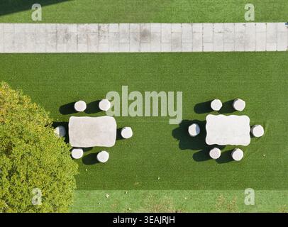 Aerial view of two stone tables and stools arranged on a vibrant green lawn next to a paved stone walkway in Taiwan. Stock Photo