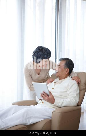wife next to a middle aged man on a lazy boy chair using tablet PC Stock Photo