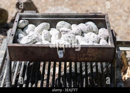Close up of white grilling stones in a rustic metal barbecue box under natural light. Organic texture background for outdoor lifestyle design. Stock Photo