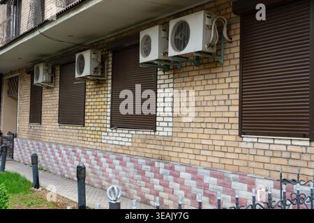 Multiple air conditioning units mounted on a brick building wall with closed shutters. Urban infrastructure concept related to cooling systems and bui Stock Photo