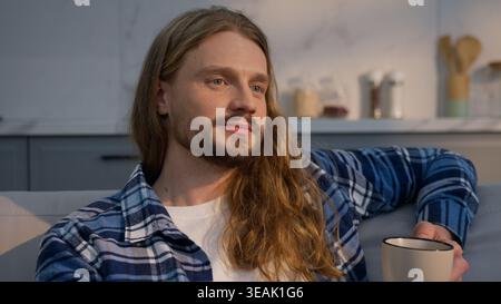 Calm relaxed Caucasian man at new rental apartment kitchen male resting enjoying tea coffee holding cup beverage thoughtful peaceful guy considering Stock Photo