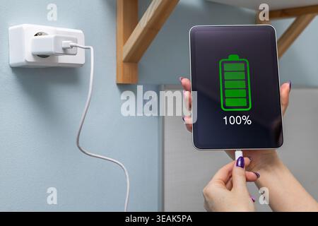 Close-up of a woman's hands charging a tablet, using a cable and USB port. A woman's hand disconnects the charging cable from a tablet. a fully charge Stock Photo