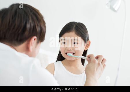 Portrait of girl brushing her teeth smiling at her father Stock Photo